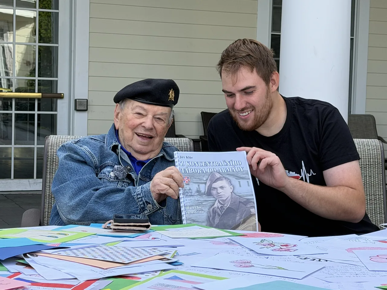 Historian Jiri Kluc and Holocaust survivor and WWII veteran Harry Arnstein holding a book about Arnstein’s life, surrounded by letters and drawings.
