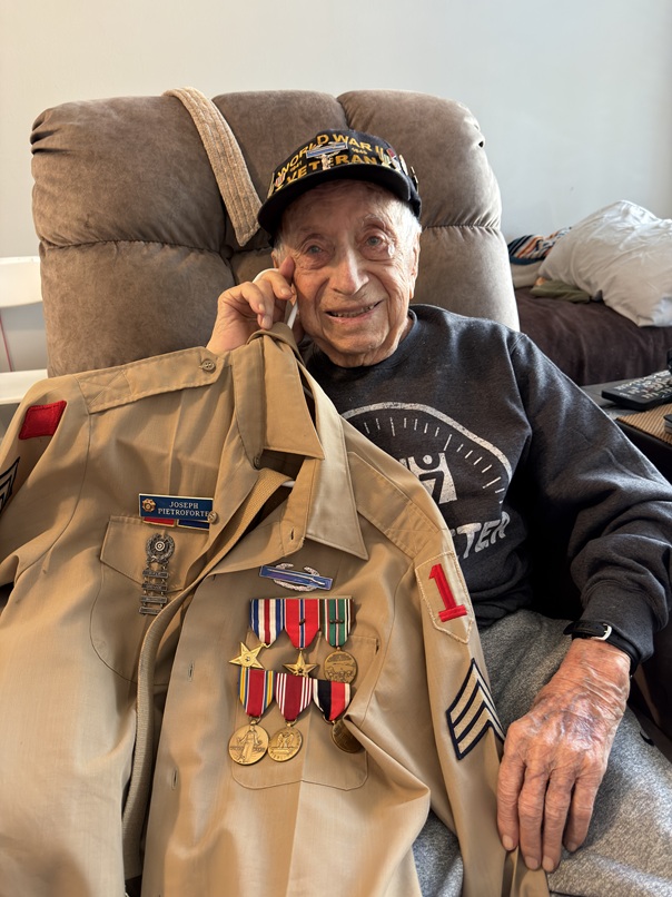 Joseph Pietroforte holding his U.S. Army uniform with medals and insignia.