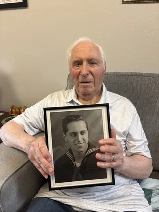 Abe Laurenzo holding a framed photograph of himself in United States Navy uniform.