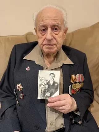 Arkady Gorbunov wearing his military decorations and holding a wartime portrait.