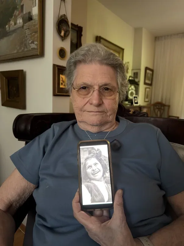Daisy Gross holding a phone displaying a photograph of herself as a child.