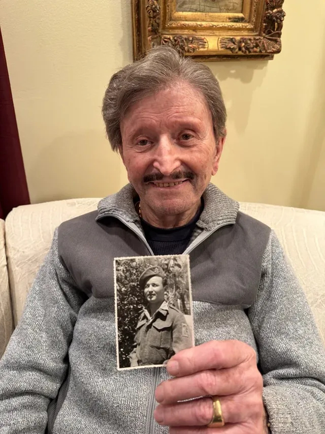 David Karmi holding a photograph of himself in military uniform.