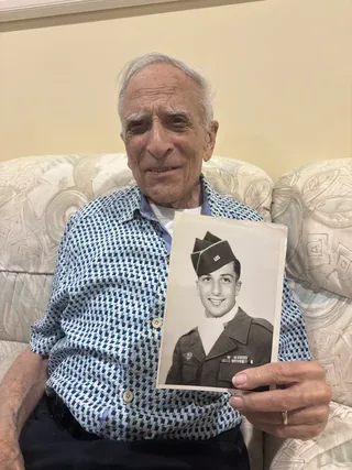 Frank Cohn holding a photograph of himself in US Army uniform.