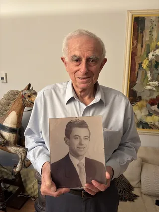 Fred Schoenfeld holding a portrait photograph of himself as a young man.