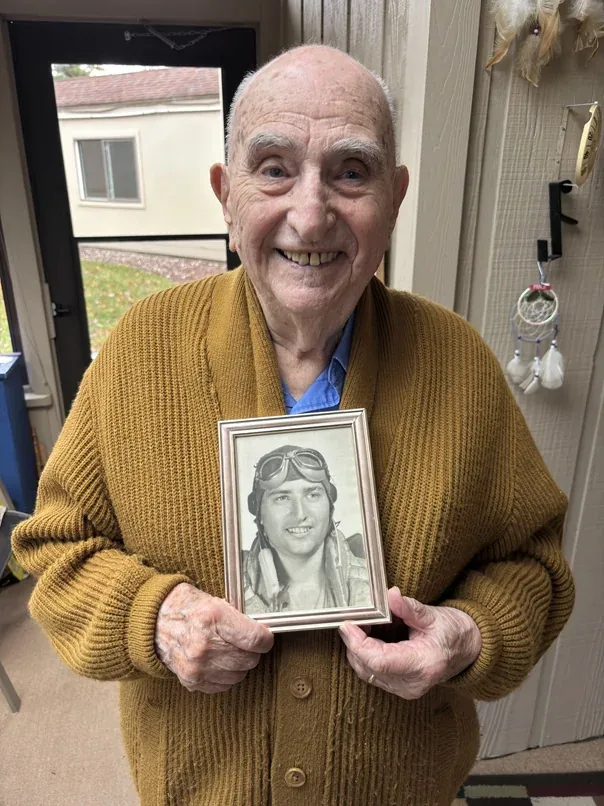 George Rubin holding a framed portrait of himself as a young airman.