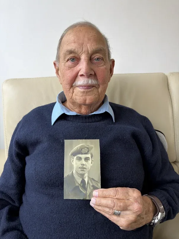 Herman van der Leelie holding a photograph of himself in military uniform.