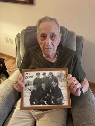 Quentin Stambaugh holding a framed wartime photograph of his bomber crew.