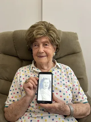 Ruth Mermelstein holding a phone displaying a photograph of herself as a young woman.
