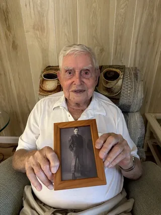 William Keegan holding a framed photograph of himself in military uniform.